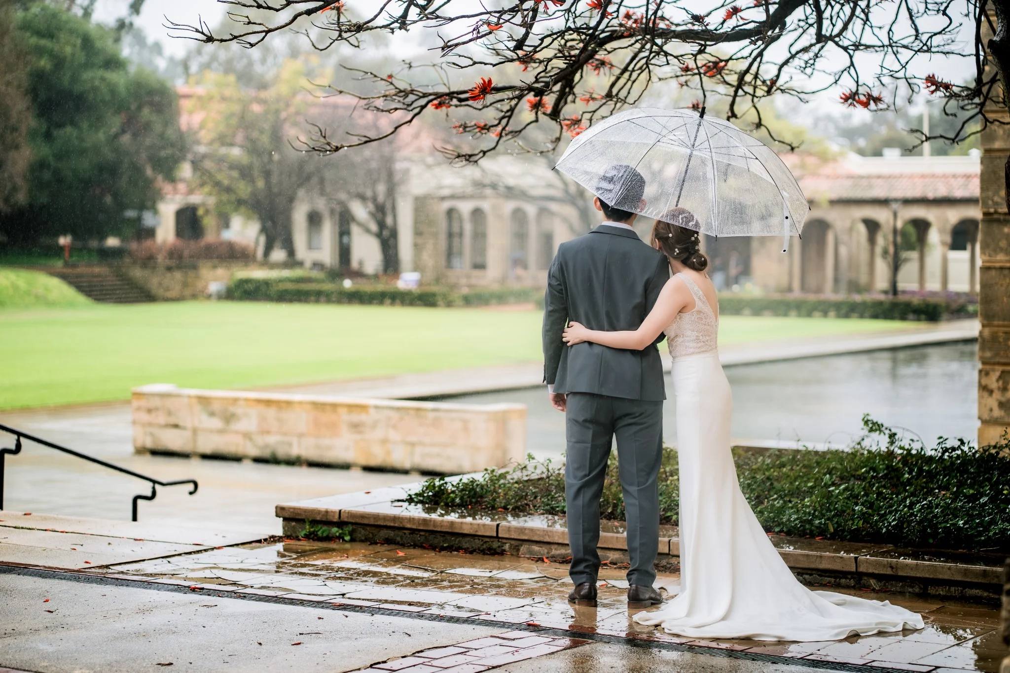 Melody and Ken beneath umbrellas on the rainy UWA campus in Perth, Western Australia