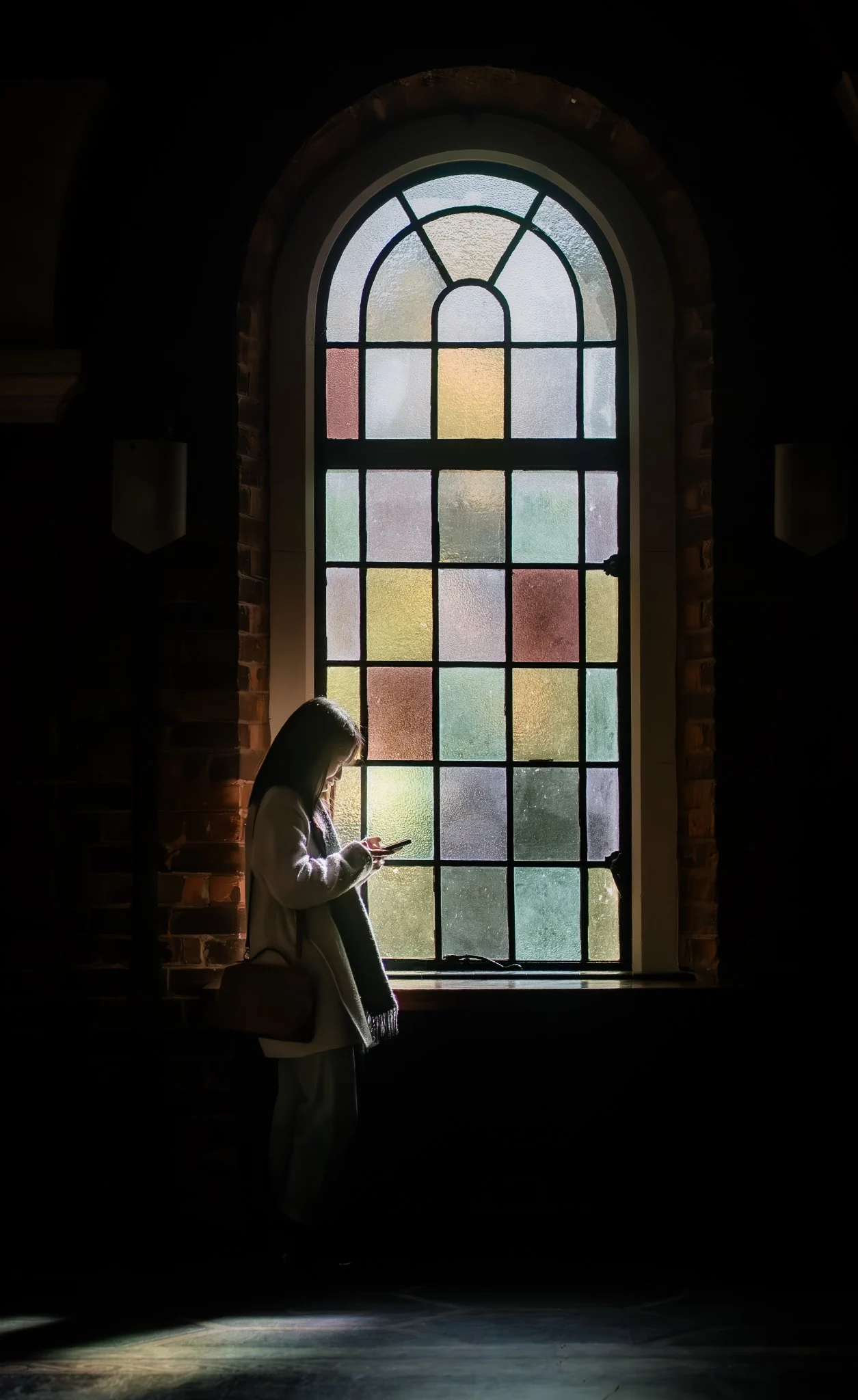 Person standing beside a stained-glass window illuminated by coloured light